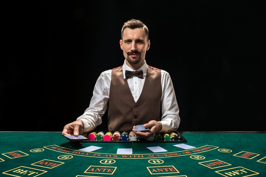 A croupier with a beard and mustache stands behind a casino table, dealing cards out in front of him. BetMGM Casino Ontario offers a great selection of fun & exciting live dealer games, bringing all the live casino action to you in your home