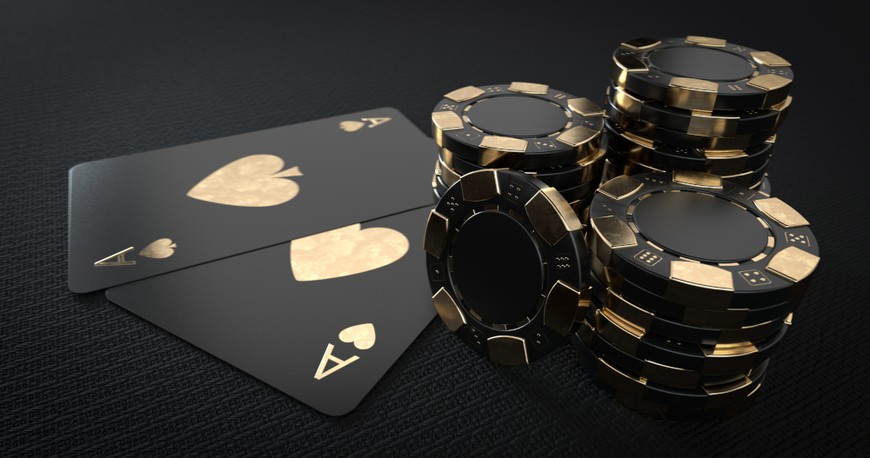 Black and gold poker chips and black and gold playing cards are seen on a black background.
