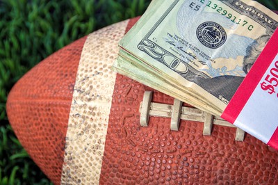 a football with a stack of bills sits on top of grass field.