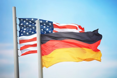 a US Flag and a German Flag are seen against a blue sky. USA vs. Germany Soccer Prediction & Match Preview