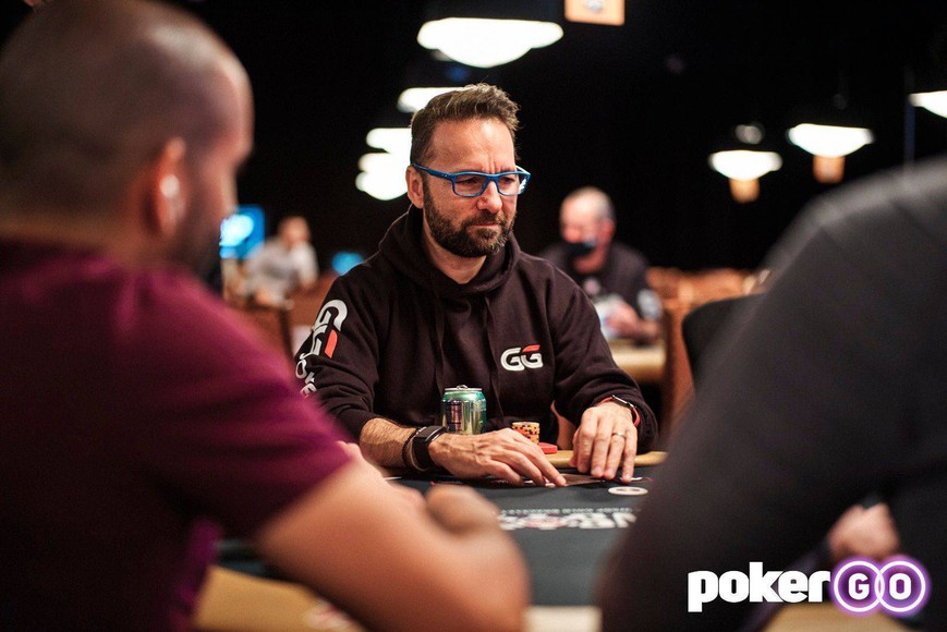 Daniel Negreanu, the Toronto-born lead ambassador for GGPoker, is seen at a poker table, intensely watching the cards. He wears blue glasses, a GGPoker hoodie, and a short beard.