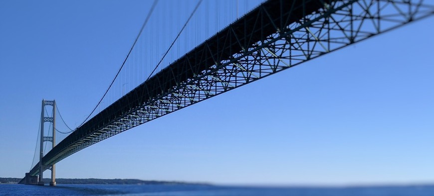 Mackinac Bridge is seen stretching over blue water and against blue skies. The Mackinac Bridge is a suspension bridge spanning the Straits of Mackinac, connecting the Upper and Lower peninsulas of the U.S. state of Michigan.