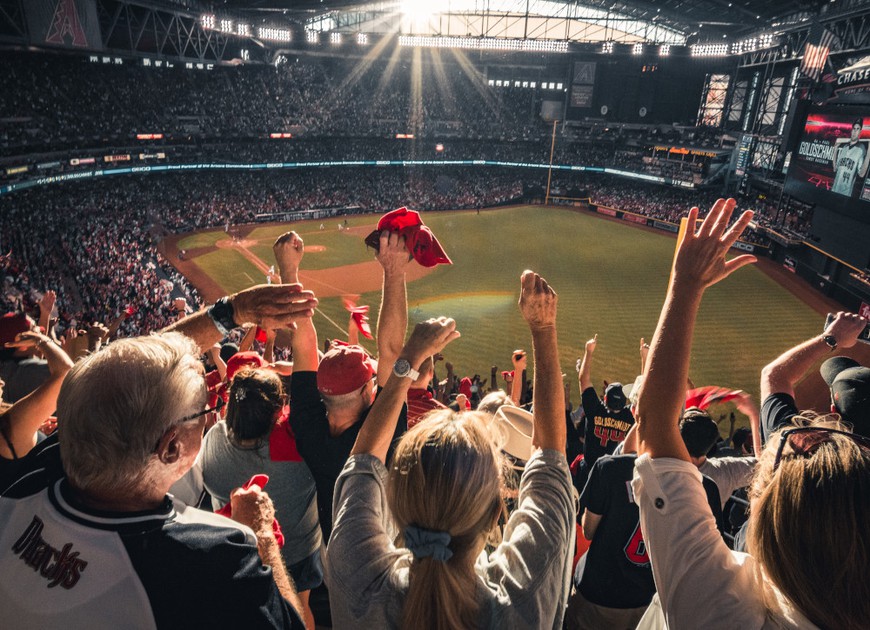 a crowd of people cheering at a baseball game. seen from the bleachers looking down at the field, they cheer and wave hands to celebrate a homerun.