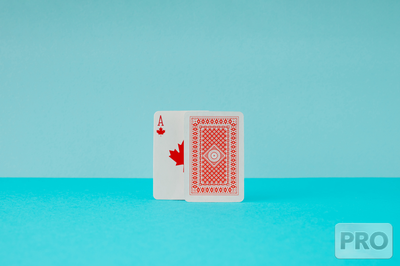 two playing cards are visible on a blue background.  one is an ace with a maple leaf instead of a diamond or a heart, partially obscured by a second card with the back side.  OLG still considering online poker in Ontario, but has no launch timeline