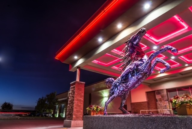 Exterior of Deerfoot Inn & Casino -- the venue for the recent (previously covid-delayed) WSOP Circuit Live Poker Tournament January 2022 -- in Calgary, Alberta, Canada. Pink neon lights shine on bottom of awning & reflect in shiny large horse sculpture