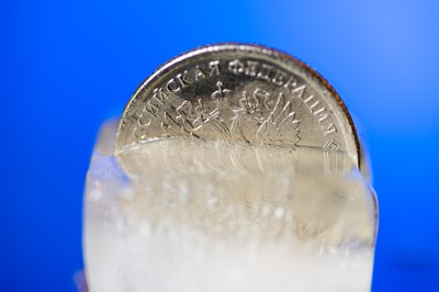 A Russian ruble coin frozen in an ice cube, against a solid blue background, representing the frozen funds on PokerStars' Sochi client, following its exit from Russia in support of Ukraine, leaving players without access to funds for the time being.