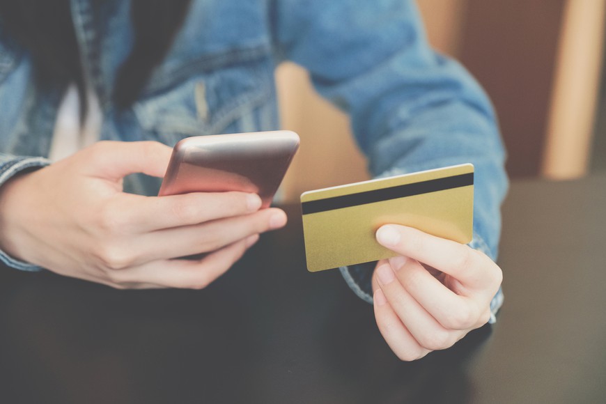 Woman holding credit card using mobile smartphone for making payment or deposit online