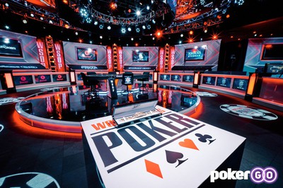 View of the World Series of Poker Final Table studio. A poker table stands on a neon-lit black platform. Neon lights and flatscreen tvs line the walls. WSOP branding is on the floors and walls.