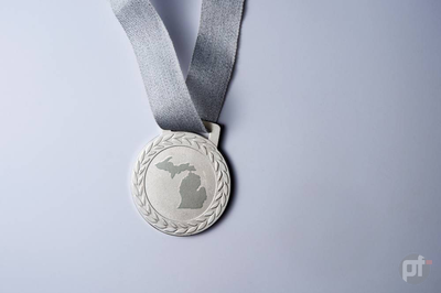 A silver medal hangs against a grey background. On the medal is the shape of the state of michigan. WSOP MI is Now the Second-Largest Michigan Online Poker Room. WSOP Michigan takes the MI silver medal and has also outpaced its Pennsylvania sibling.